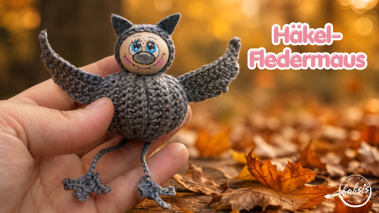 Fertige Häkelfledermaus vor herbstlichem Hintergrund mit der Aufschrift Häkel-Fledermaus.